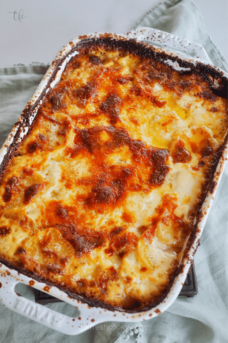 Image of baked golden brown casserole of potatoes gratin gruyere in white ceramic baking dish.