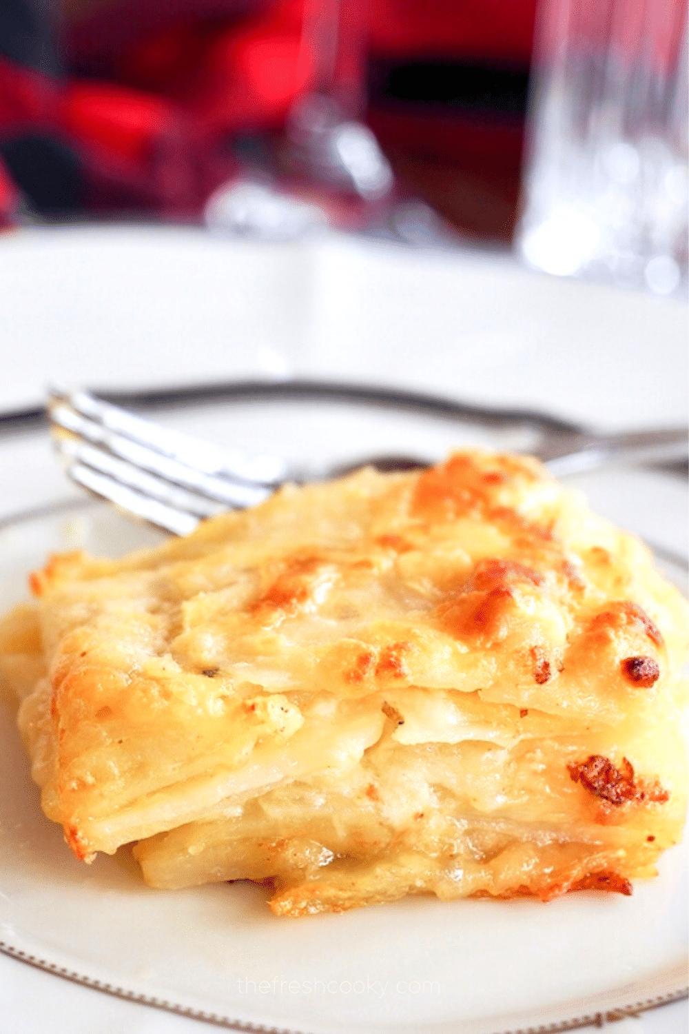 Creamy potatoes au gratin or dauphinoise potatoes on a pretty fancy plate oozing with gruyere cheese in a herb infused creamy sauce.