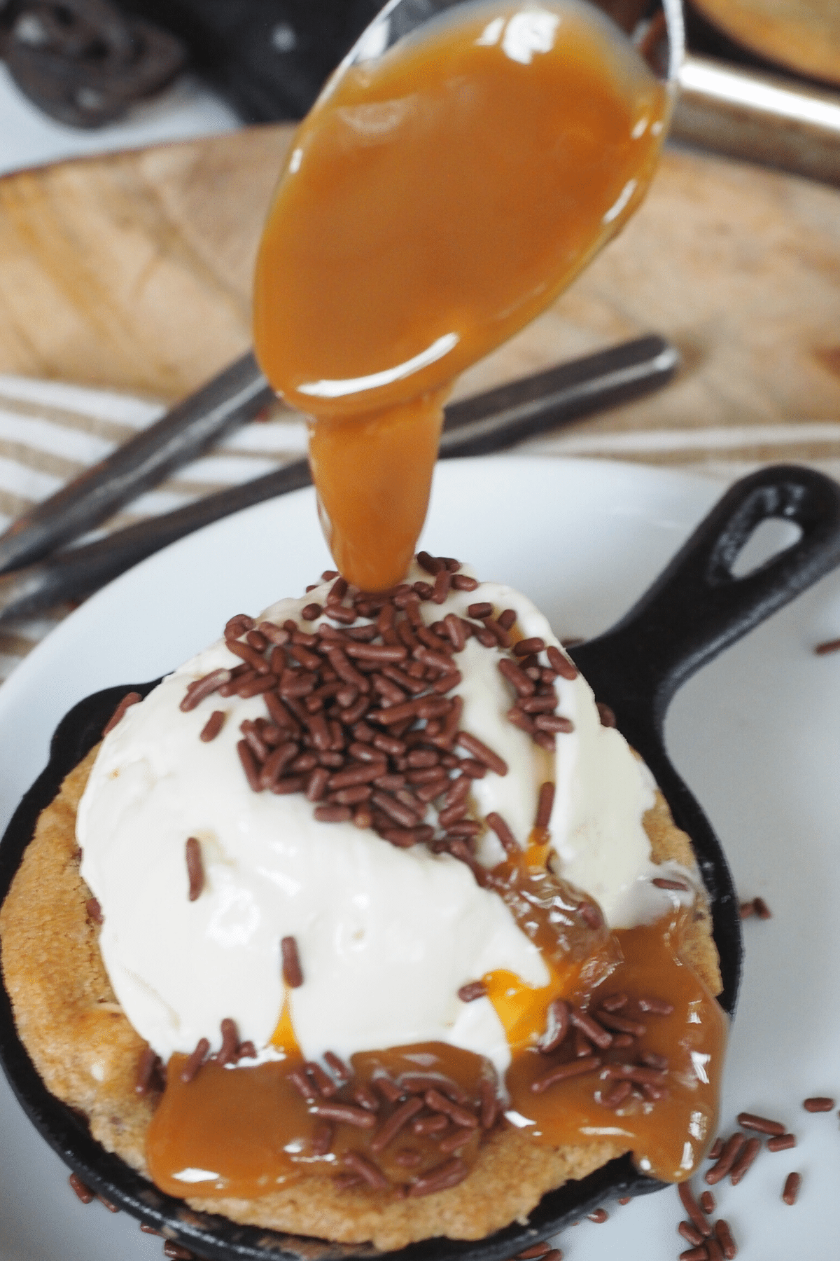 Spooning on some thick caramel syrup over the top of the mini cast iron skillet chocolate chip cookie.