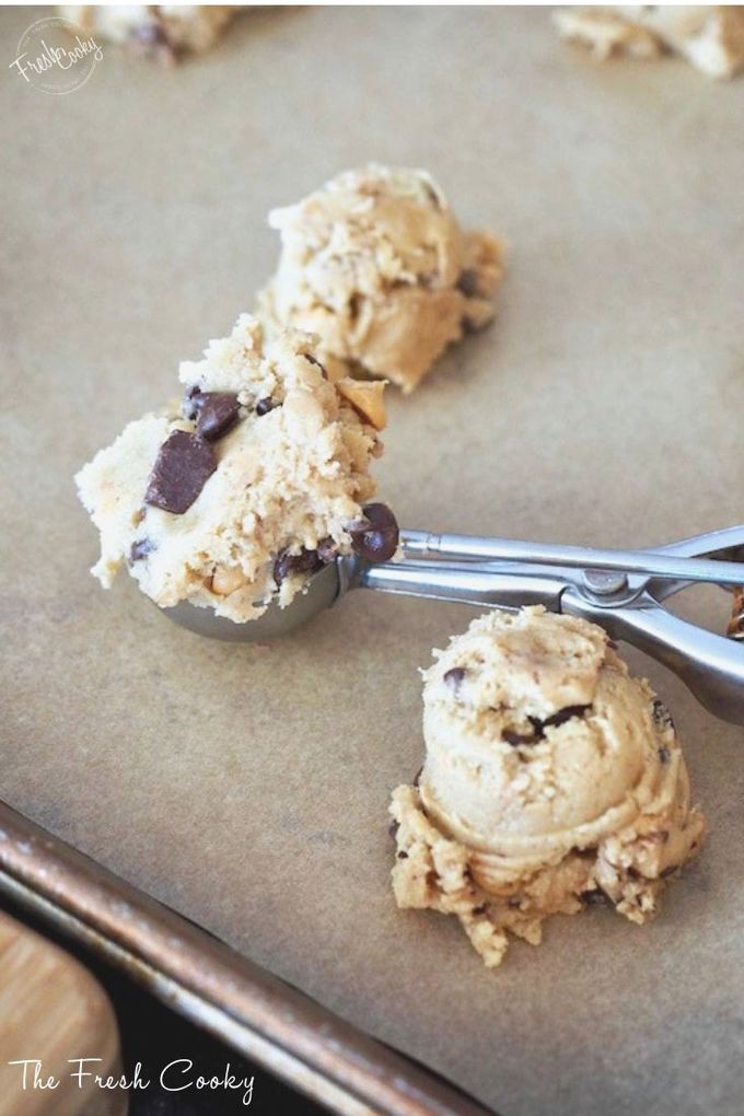 Cookie scoop sitting on parchment paper lined cookie sheet with scoops of chocolate chip cookie dough. 
