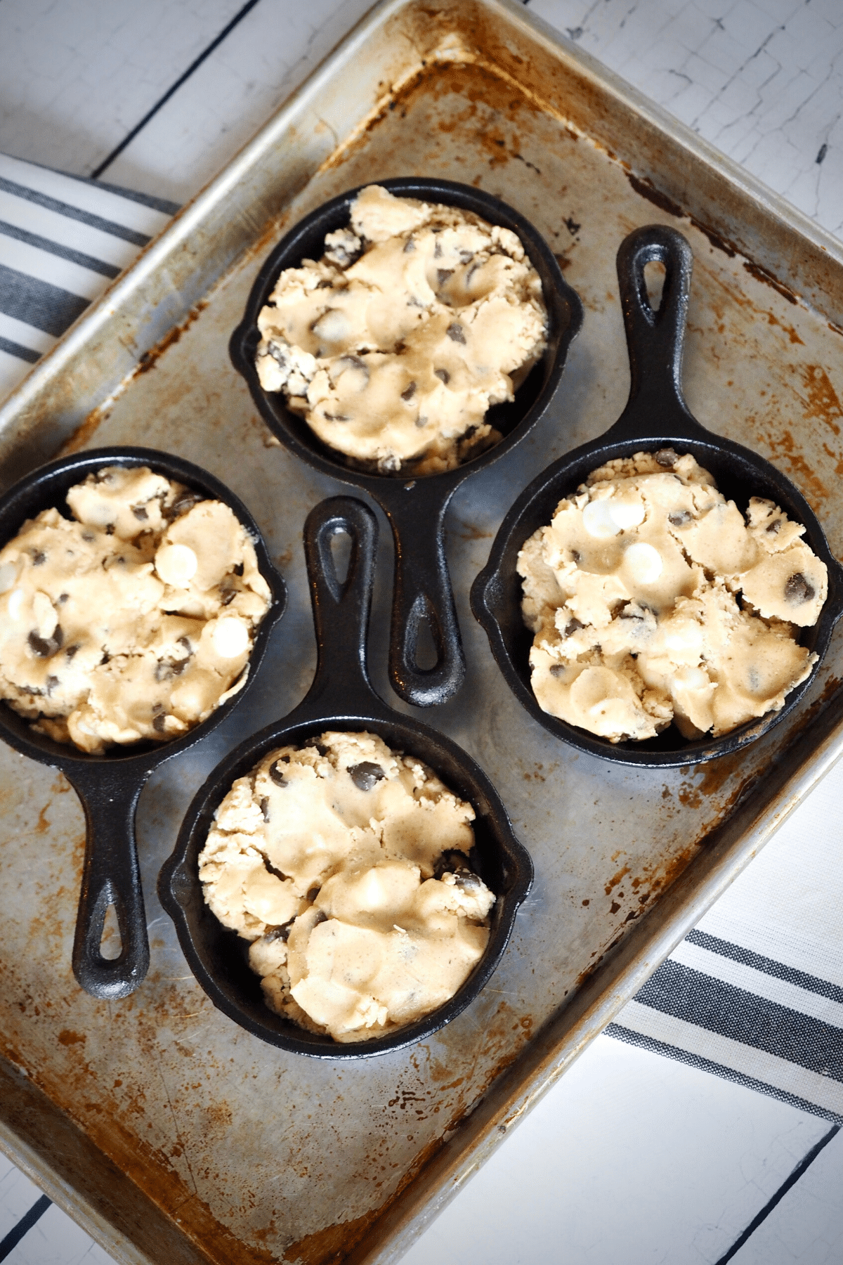 Cookie dough balls pressed into mini cast iron skillets set onto quarter sheet pan for easy baking. 