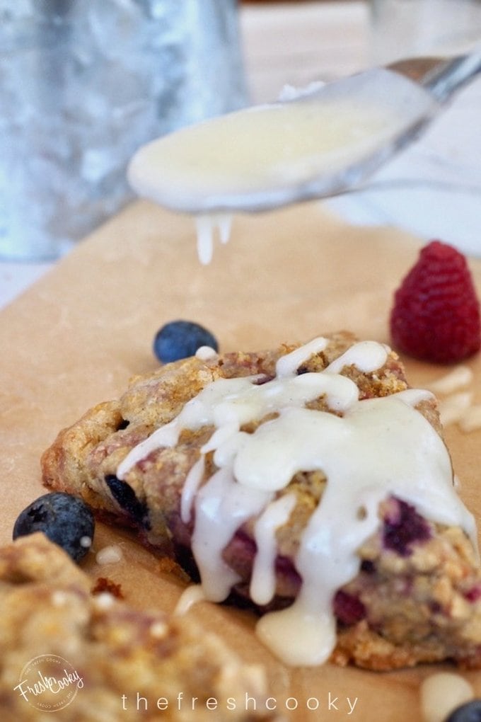 Spooning on lemon glaze for Glazed Raspberry Blueberry Scones.