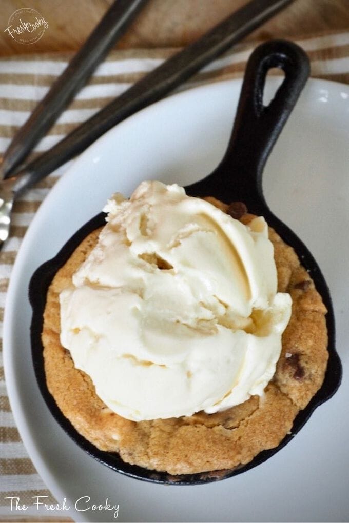 Mini skillet on white plate with scoop of vanilla ice cream on top of half baked cookie. 