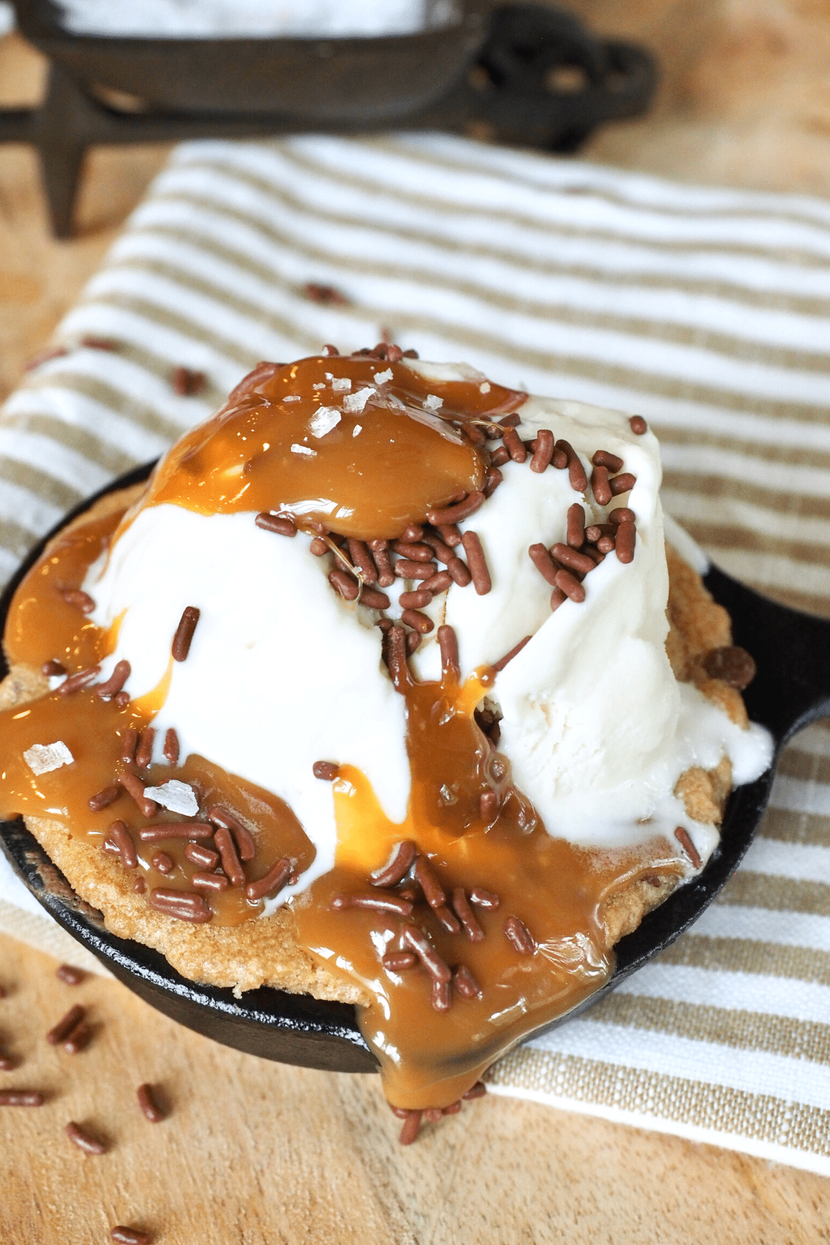 Mini Cast iron skillet chocolate chip cookie half baked recipe with ice cream and caramel syrup on top.