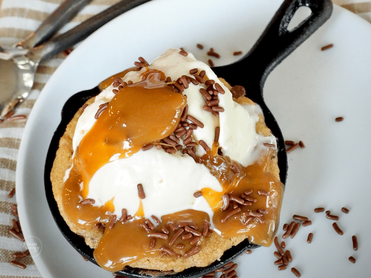Half baked skillet cookie on plate with ice cream and caramel sauce.