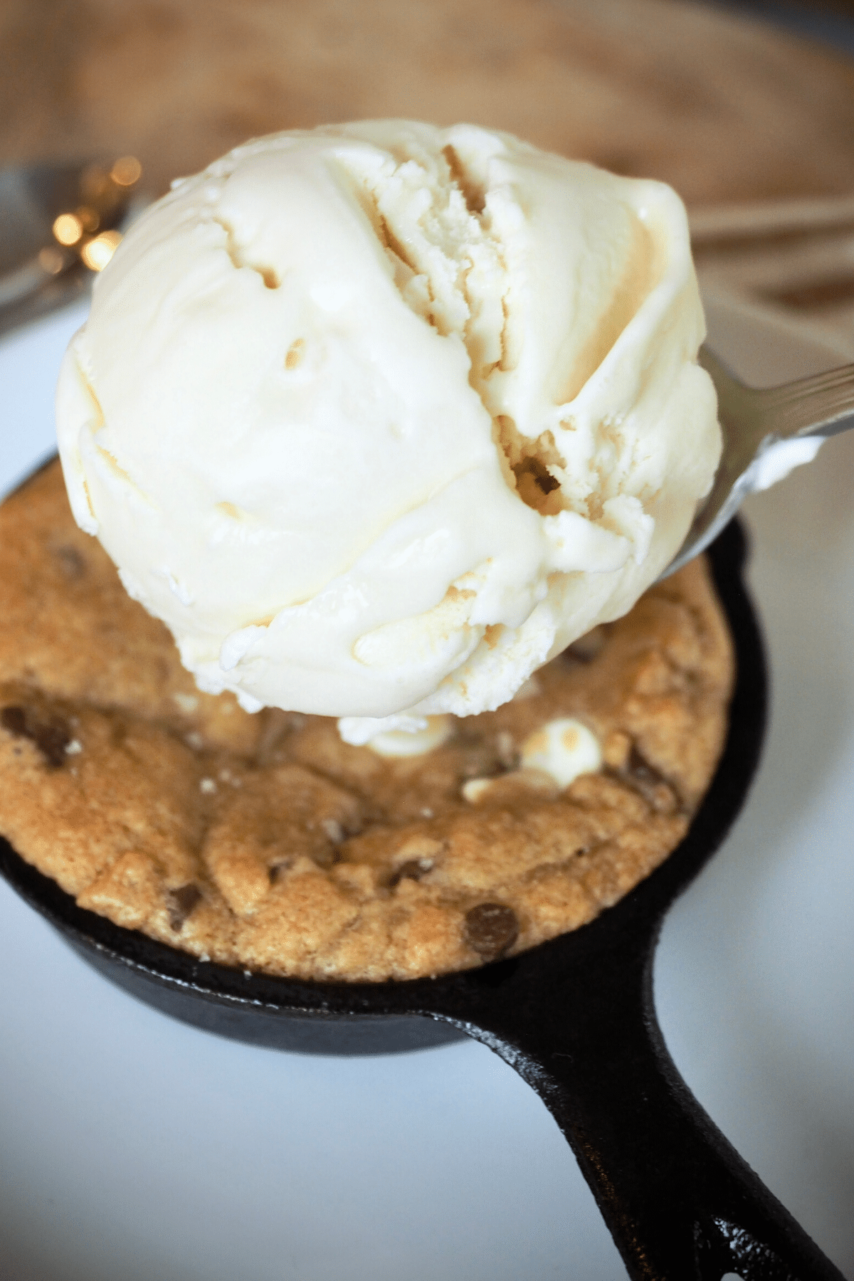Spoon placing a scoop of vanilla ice cream onto top of skillet chocolate chip cookie.