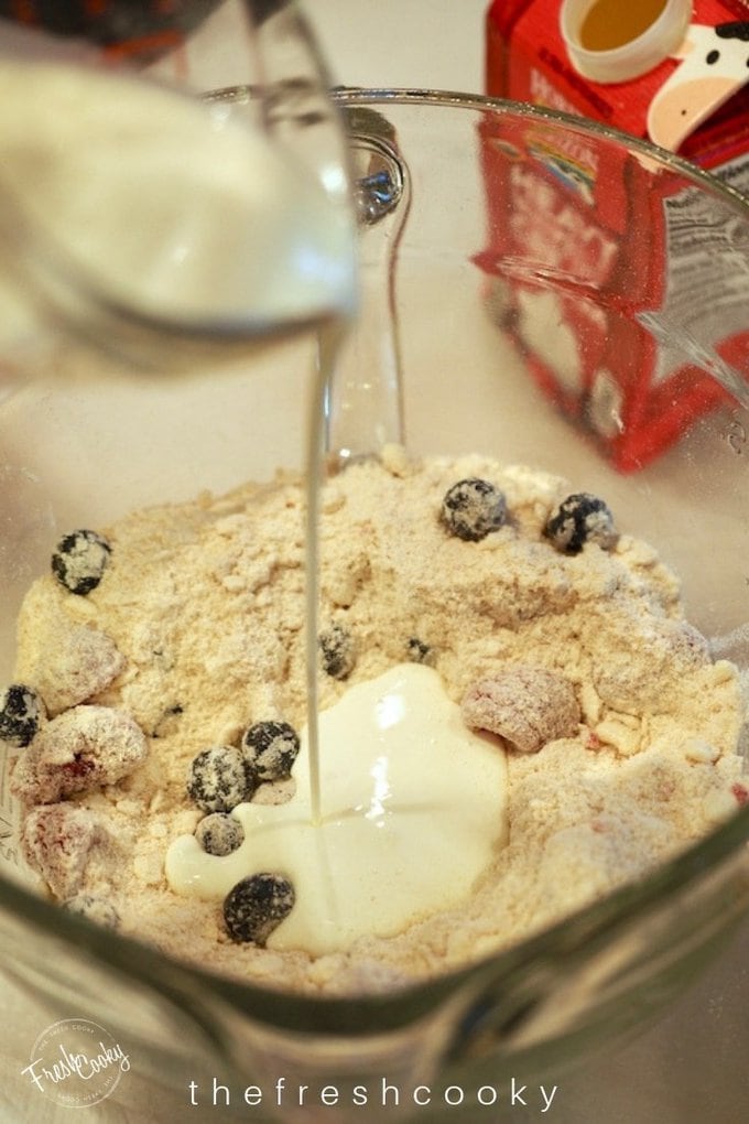 Pouring cream and egg into the Glazed Raspberry Blueberry Scones mixture. 