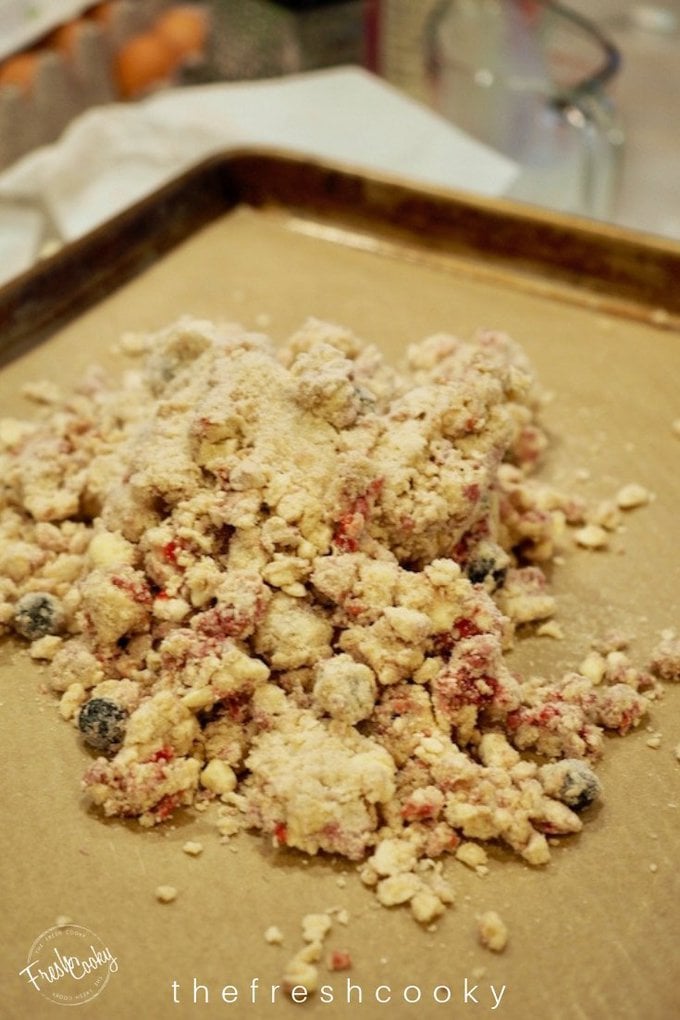 Crumbly batter on parchment paper for glazed raspberry and blueberry scones.