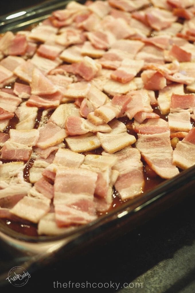 Raw pieces of bacon set on top of baked beans before baking!