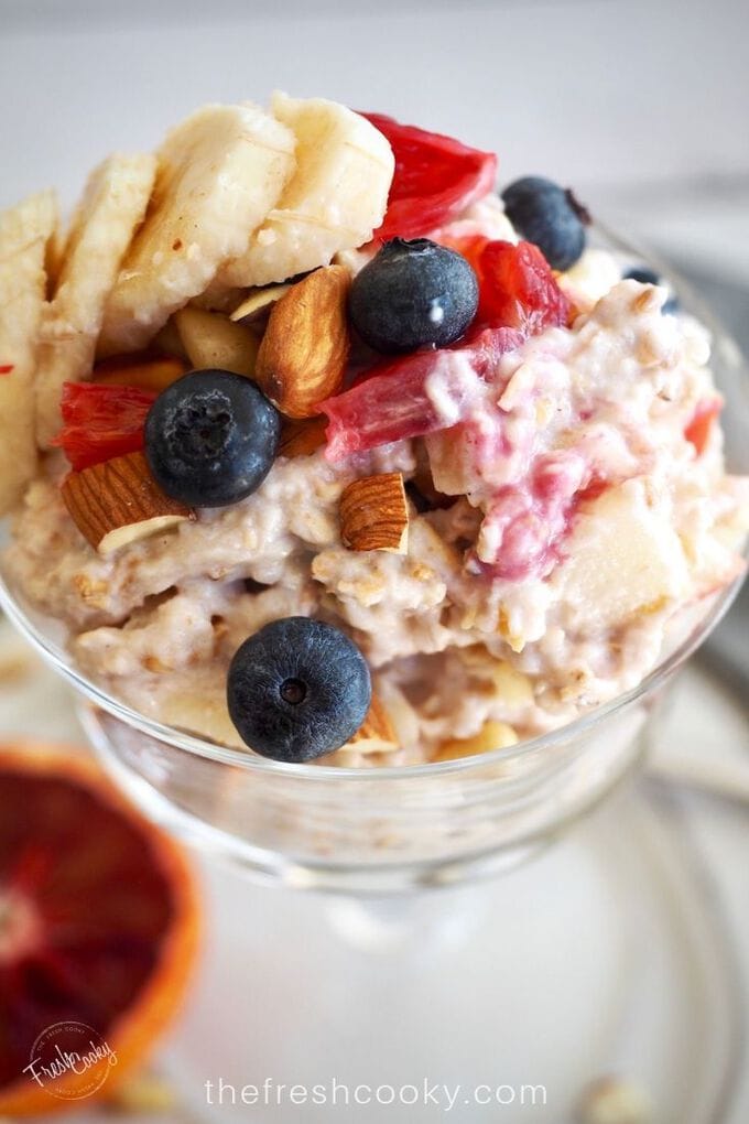 Pretty glass dish filled with bircher muesli or protein overnight oats topped with chopped nuts and fruits. 