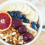 Protein overnight oats in a bowl topped with bananas blueberries, almonds, cherries and a slice of orange.