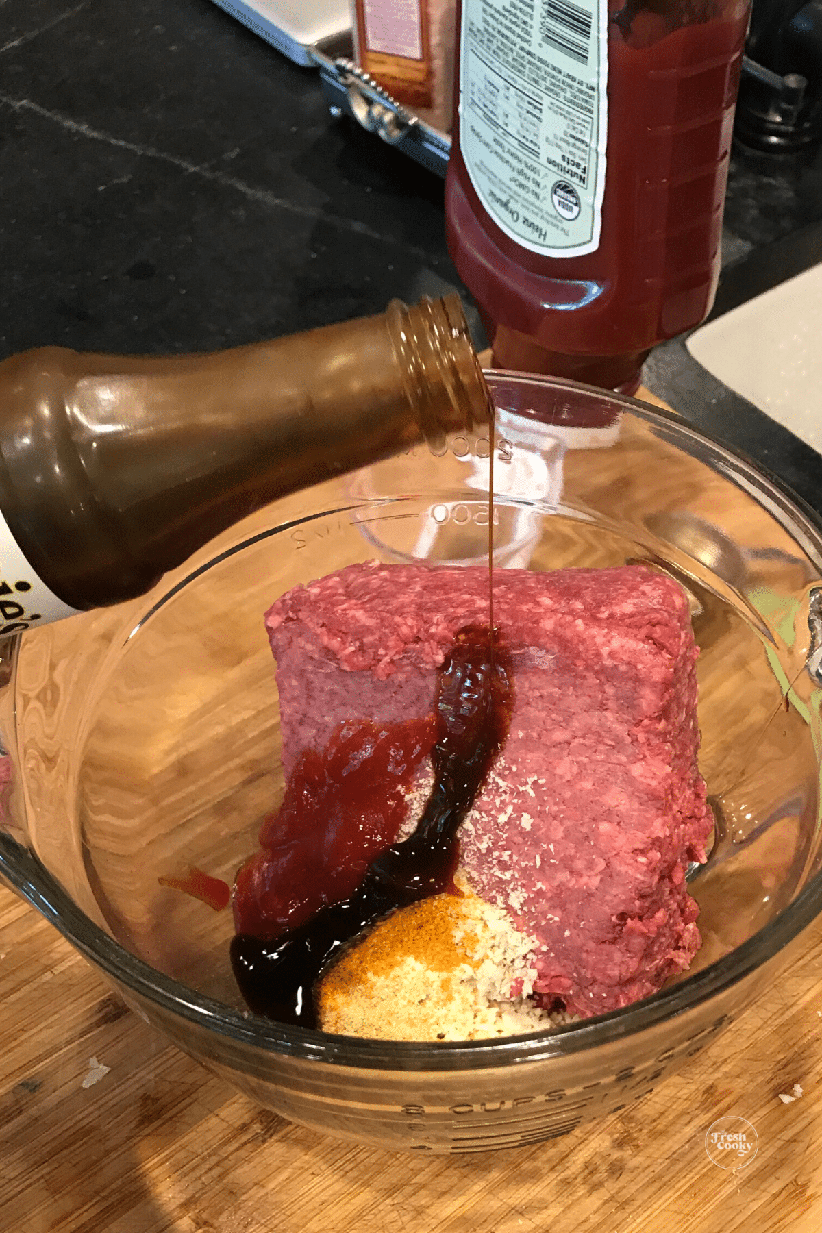 Pouring in worcestershire sauce into meat mixture.