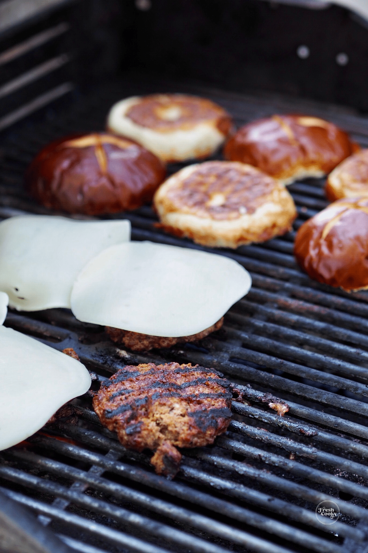 Grilling bison burgers on grill with cheese and pretzel buns.