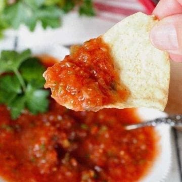 Blender salsa in a bowl, with a tortilla chip dipped in.