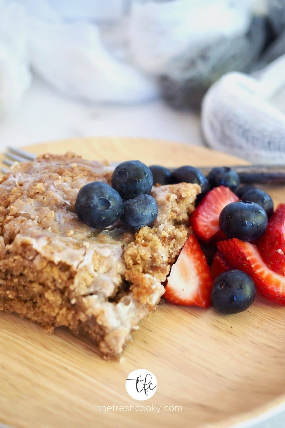 Slice of gluten free coffee cake on bamboo plate with blueberries and strawberries. 