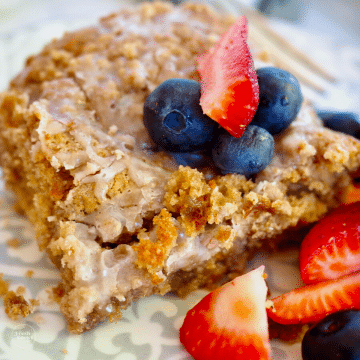 Close-up image of square of gluten-free coffee cake recipe on plate with blueberries and strawberries.