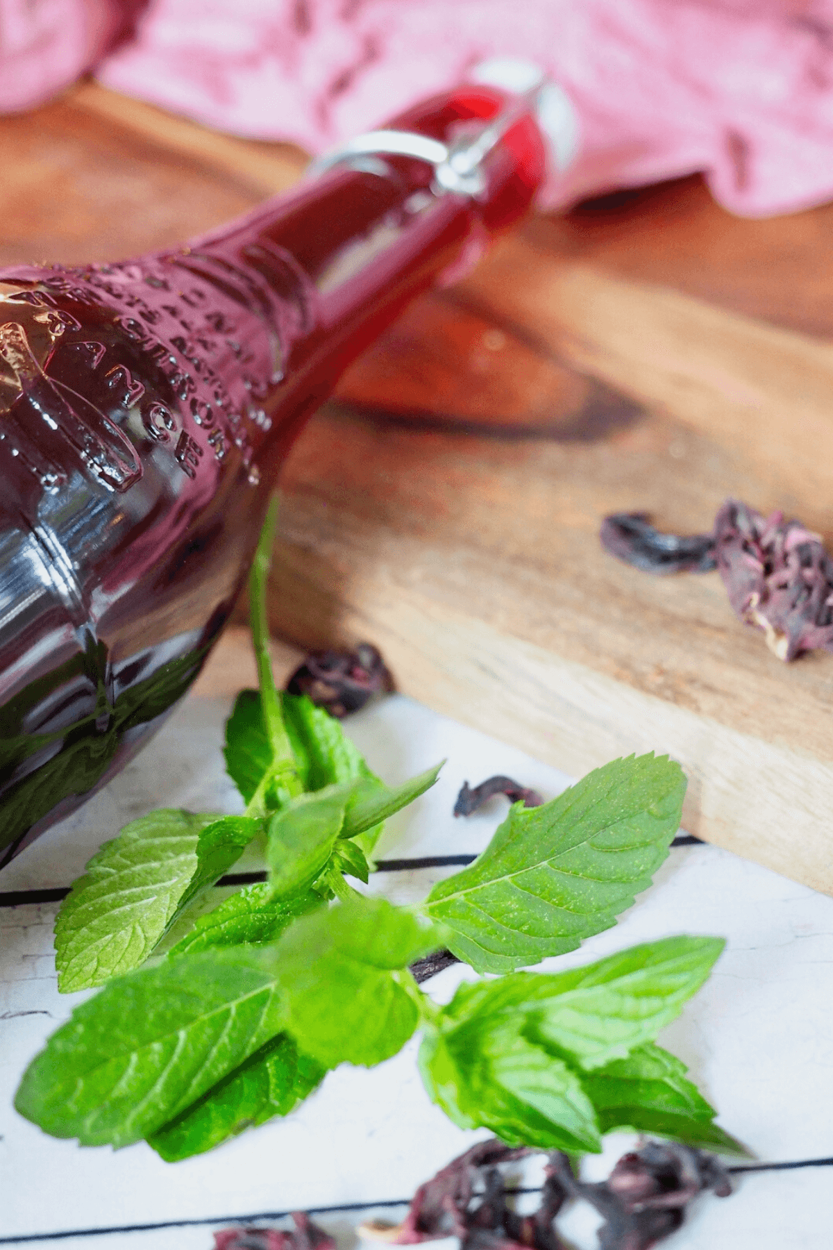 Full bottle of passion tea concentrate with fresh mint and dried hibiscus flowers nearby. 
