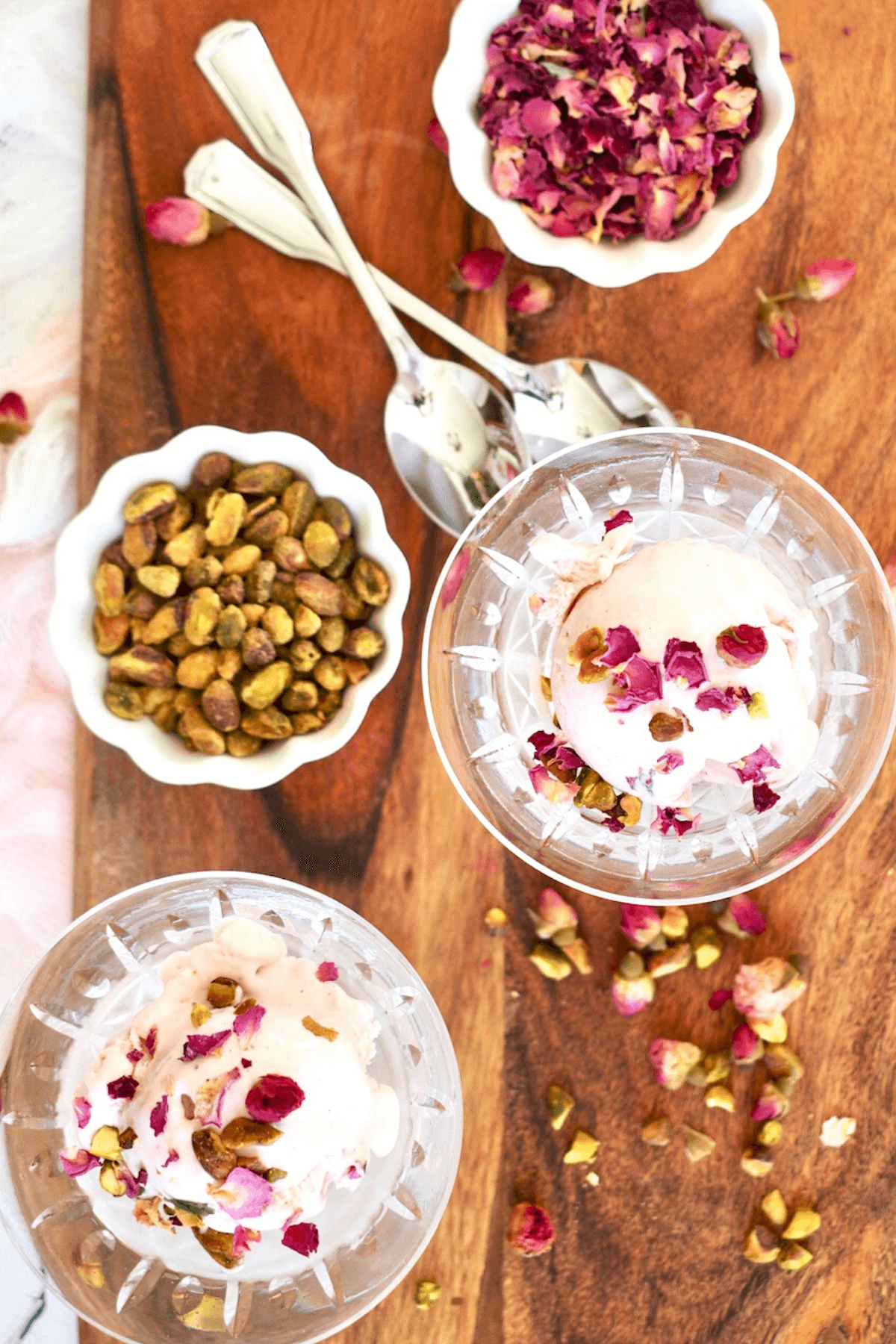 Rose Ice Cream in pretty glasses on wooden cutting board with rose petals, spoons and pistachios for garnish.