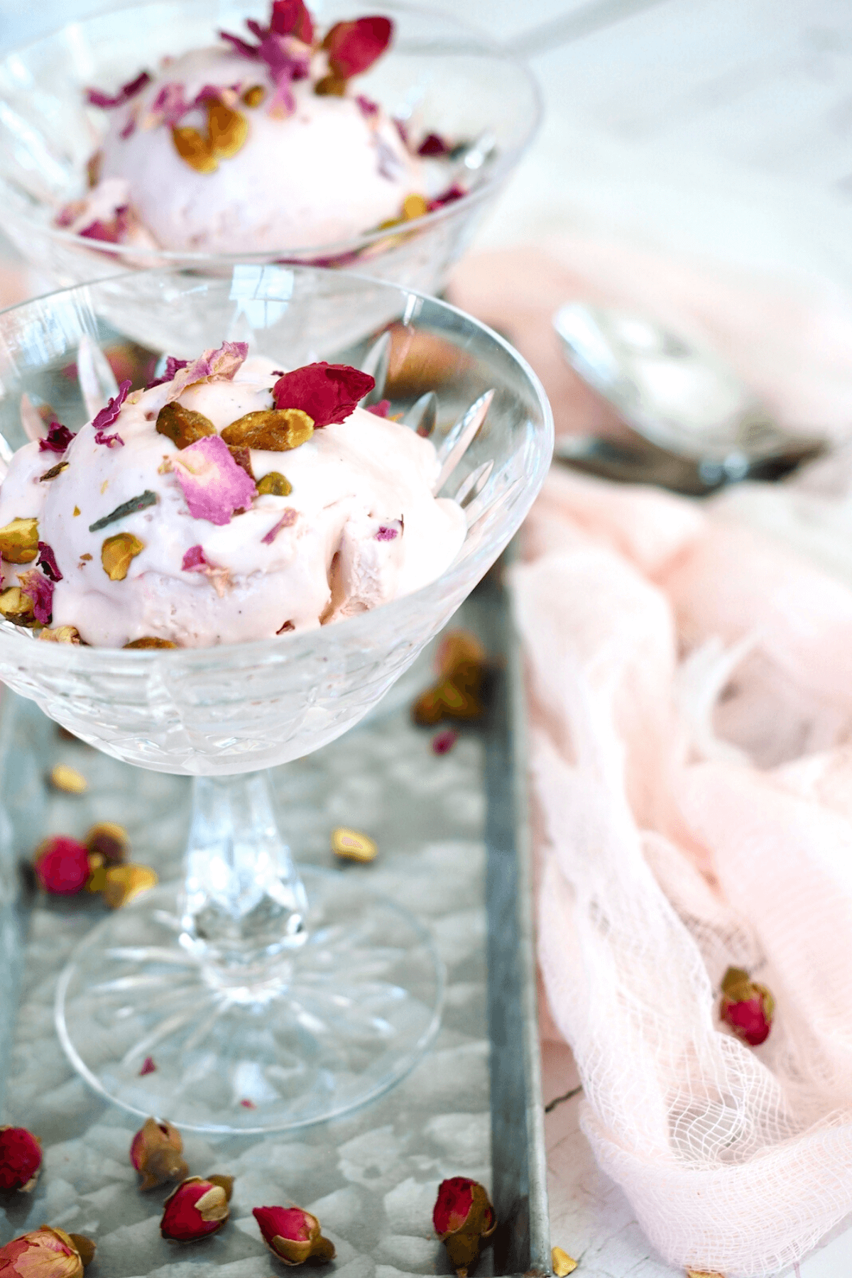 Rose ice cream in cut crystal glasses garnished with pistachios and rose petals on a pretty galvanized tray.