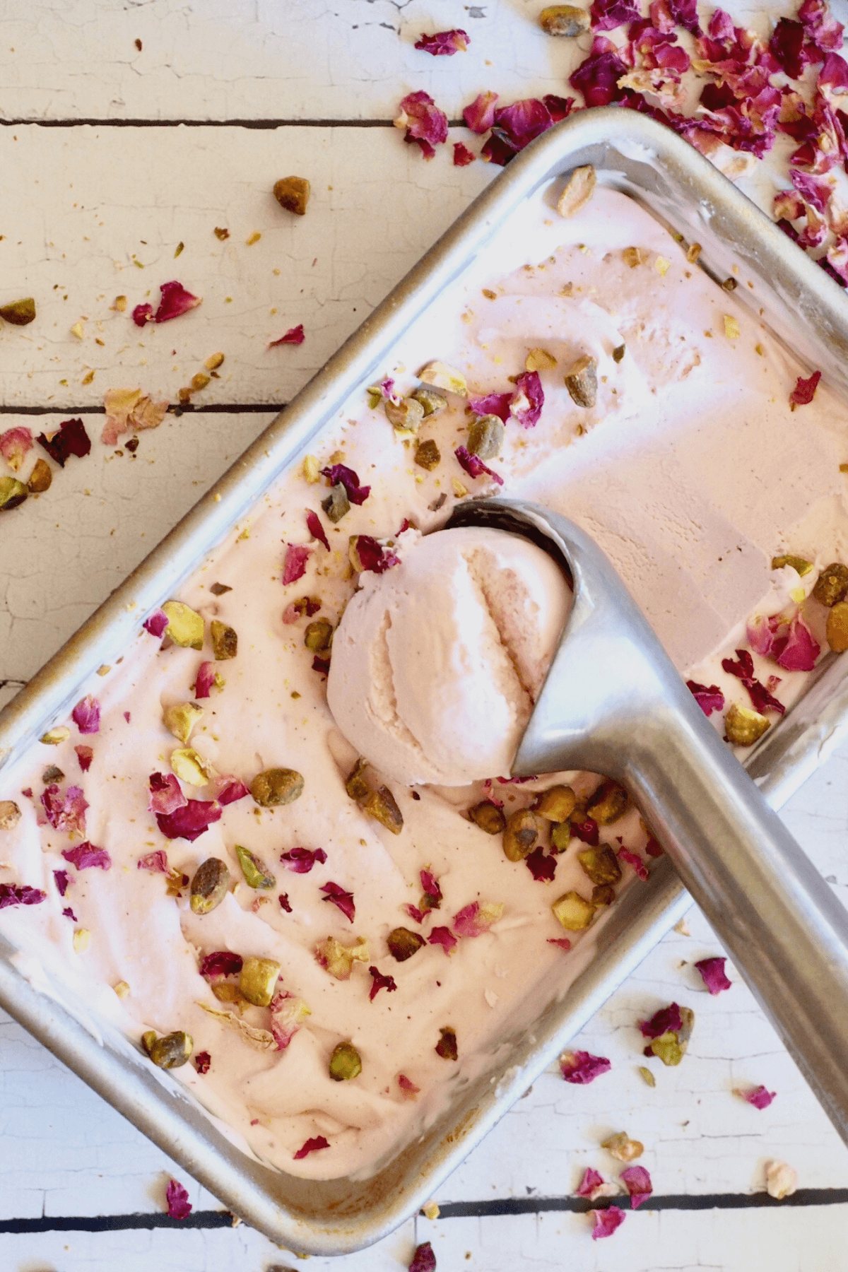 Rose ice cream in a 9x5 loaf pan with ice cream scoop scooping out a serving.