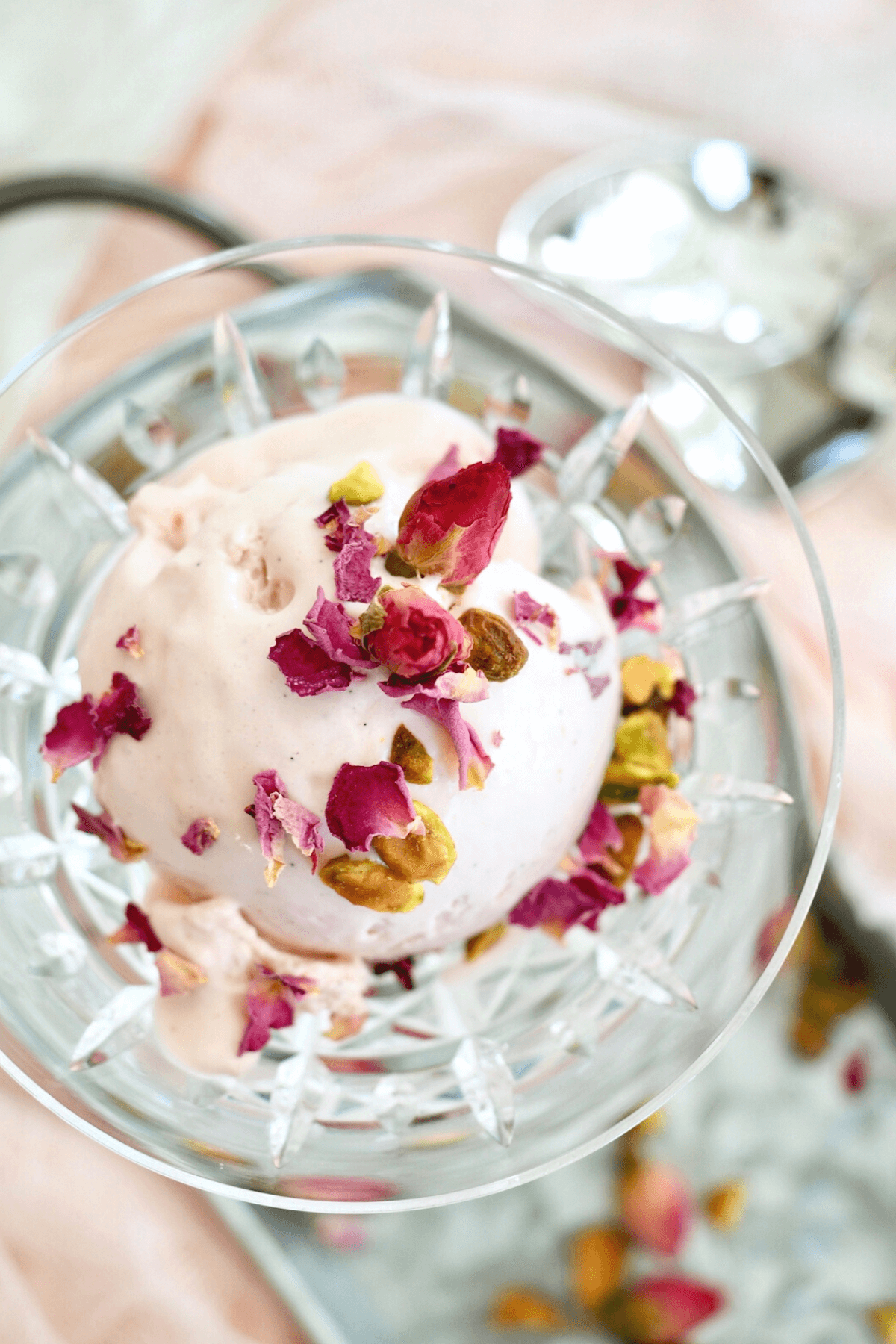 Rose ice cream scooped into cut crystal glass top down shot garnished with pistachios and dried rose petals.