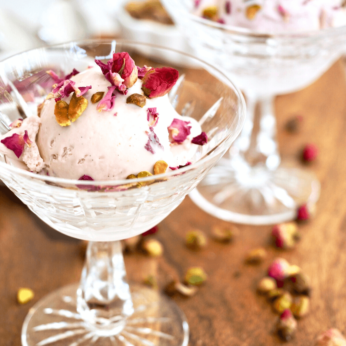 Rose Ice Cream Recipe square image with two pretty dessert dishes scooped with a scoop of pink rose ice cream, topped with pistachios and rose petals.