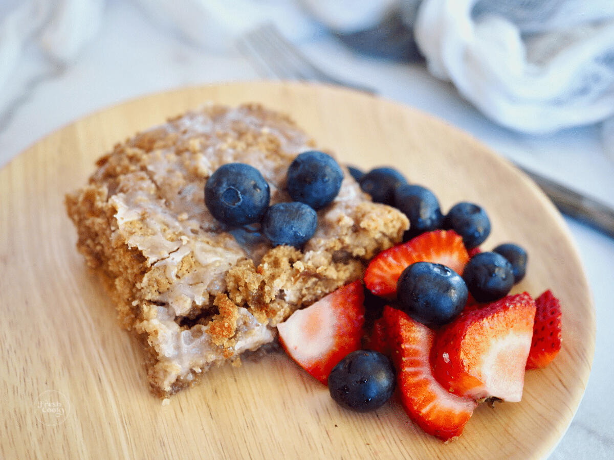 Gluten-free coffee cake on bamboo plate with fresh fruit.