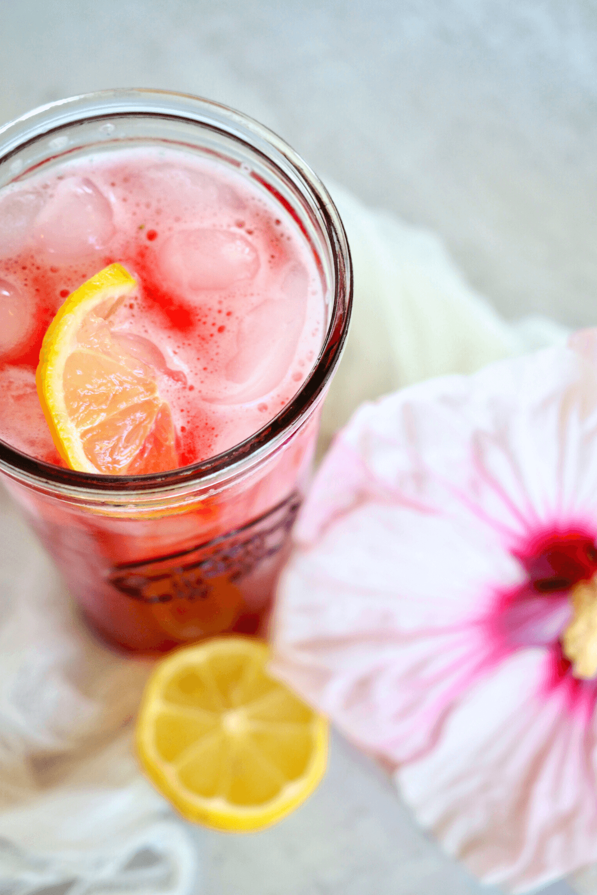 Starbuck Passion Tea Lemonade Recipe in glass Starbuck's cup with fresh hibiscus flower and slice of lemon.