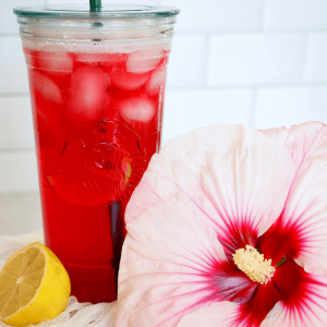 Starbucks Passion Tea Lemonade in glass starbucks cup with fresh hibiscus flour and half of lemon.