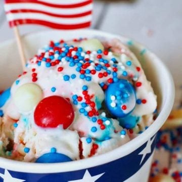 Scoop of red, white and blue ice cream with American flag and sprinkles in a patriotic cup.