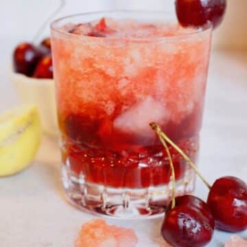Cherry Bomb Cocktail in pretty glass with cherries and lemon nearby.