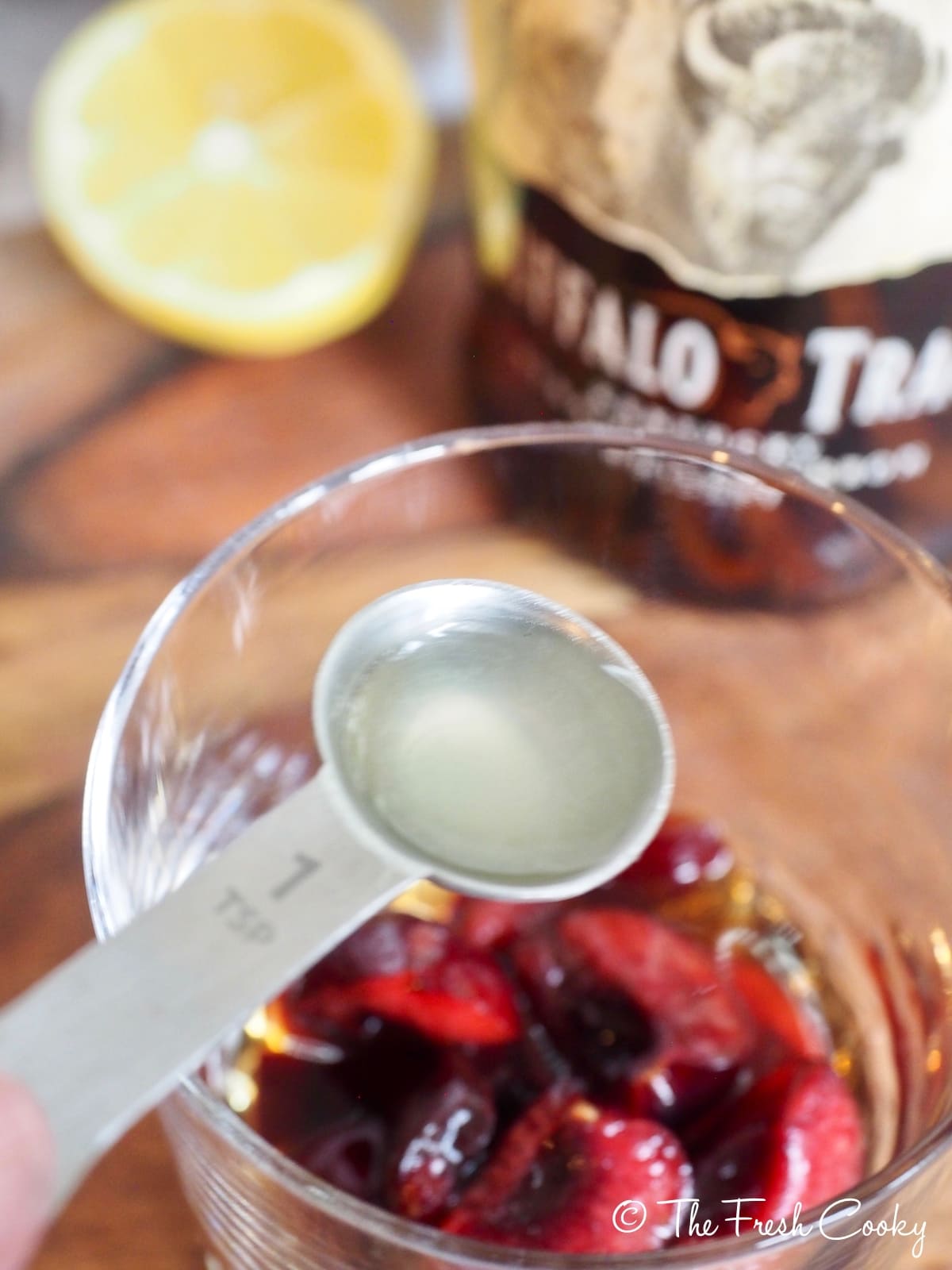 Teaspoon of fresh lemon juice being added to Cherry Bomb Cocktail.