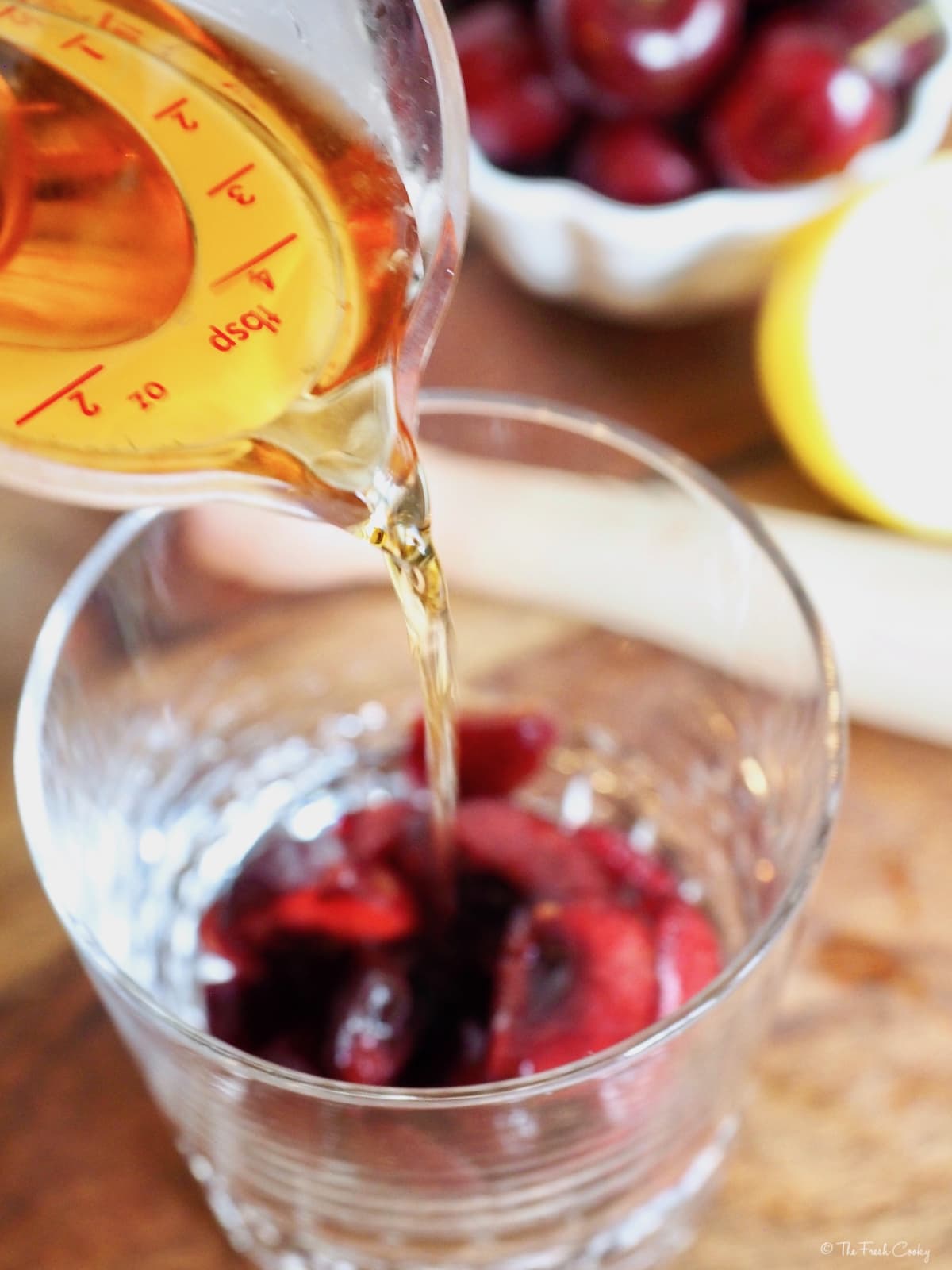 Pouring whiskey into glass of muddled cherries for Cherry Bomb Cocktail.