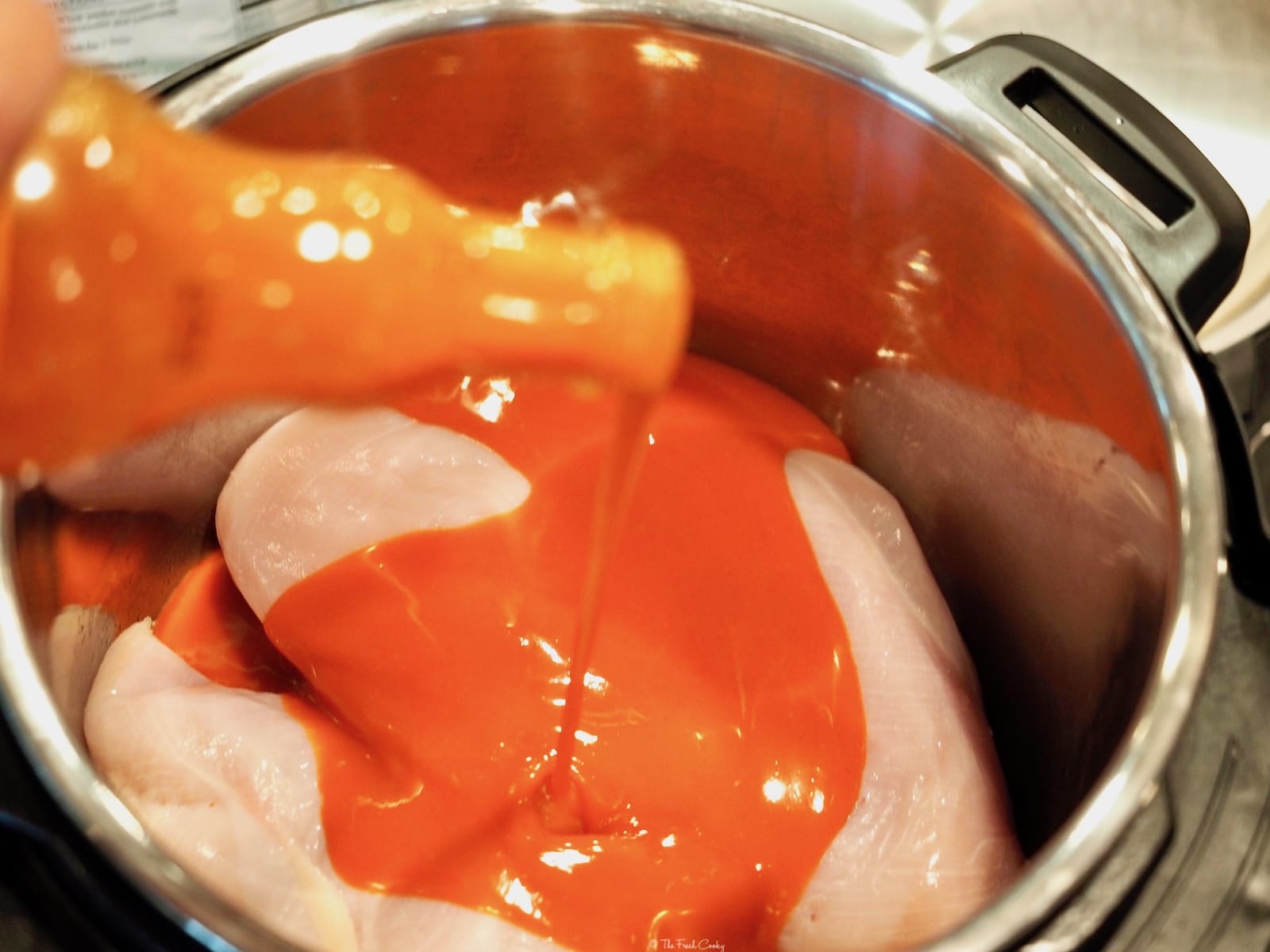 Instant Pot with raw chicken breasts, pouring Frank's Buffalo Hot Sauce on the top | thefreshcooky.com