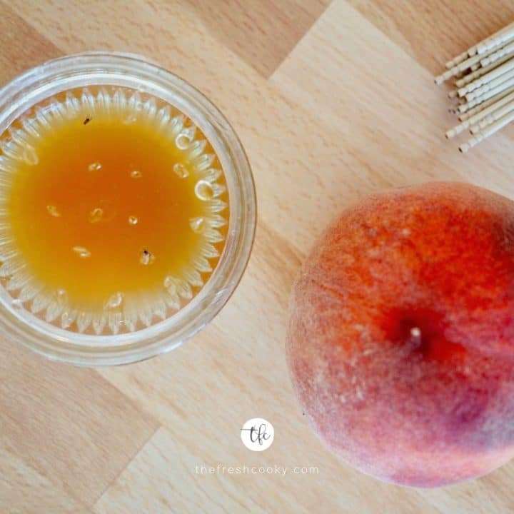 Square image of fruit fly trap with dead fruit flies or gnats in the trap with a peach nearby.