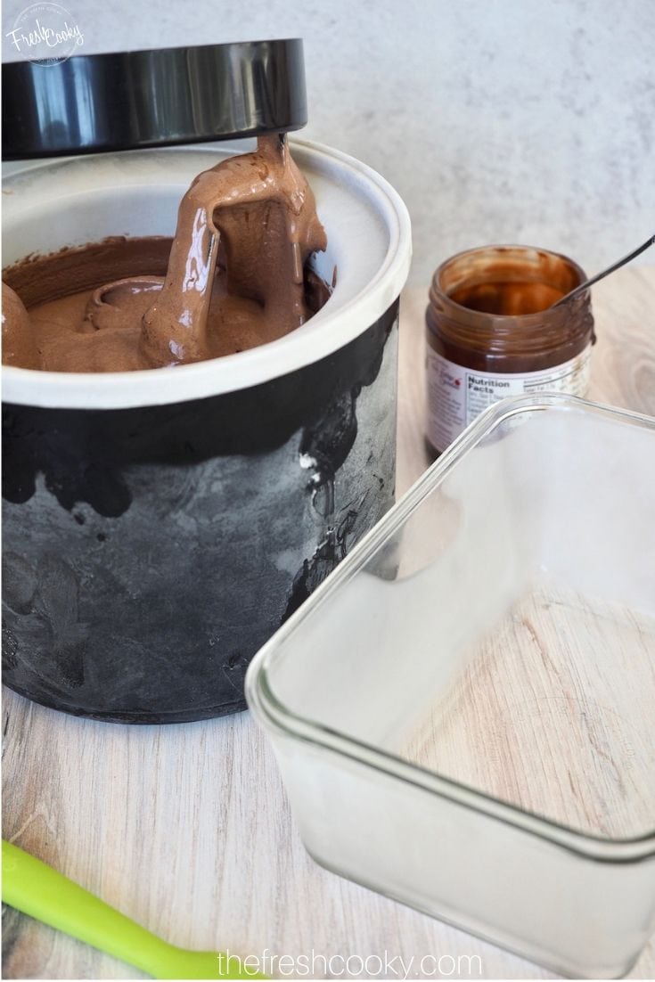 Frozen glass dish with freezer container filled with Chocolate Ice cream and jar of chocolate sauce in background.