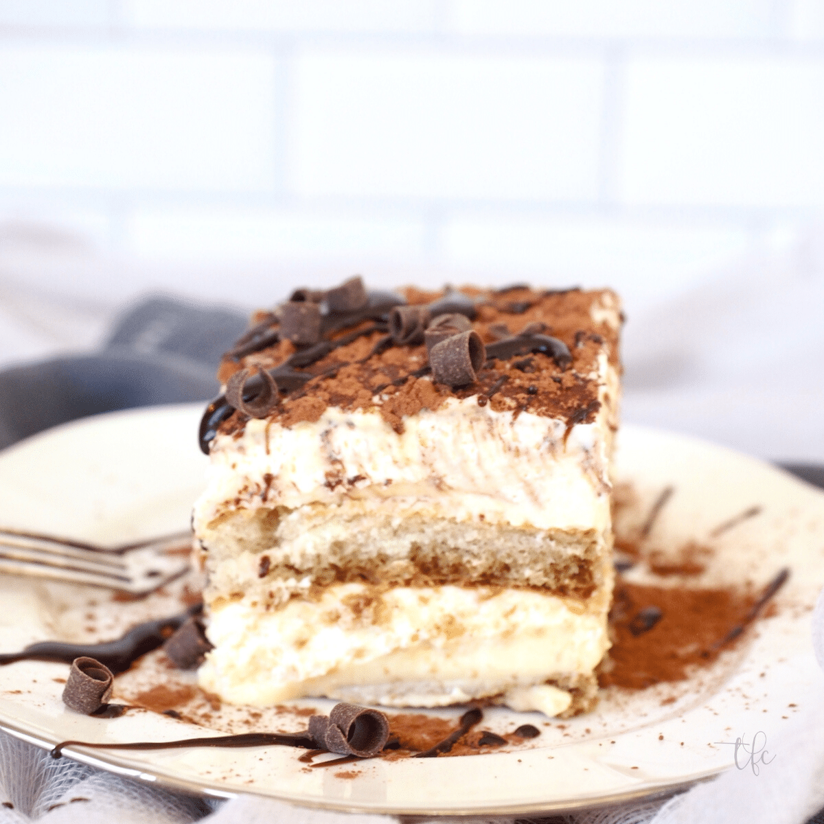 Tiramisu slice on a plate sprinkled with cocoa powder and a drizzle of chocolate sauce.