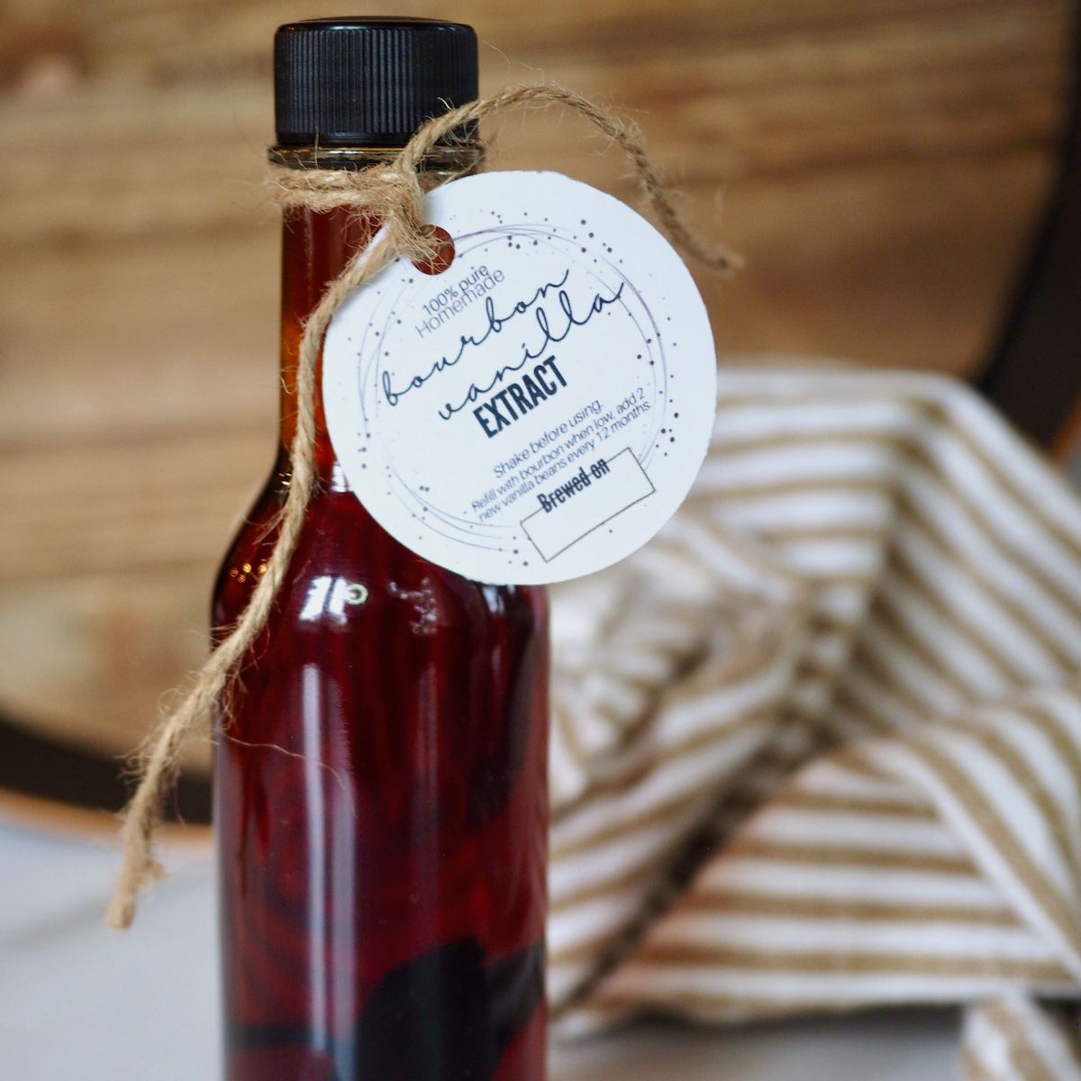 A small glass bottle filled with dark bourbon vanilla extract tied with a printable label.