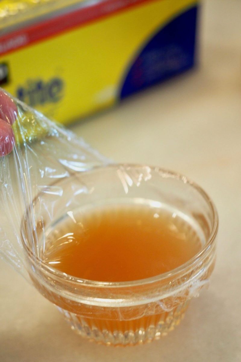 Pulling plastic wrap taught across the top of the apple cider vinegar.