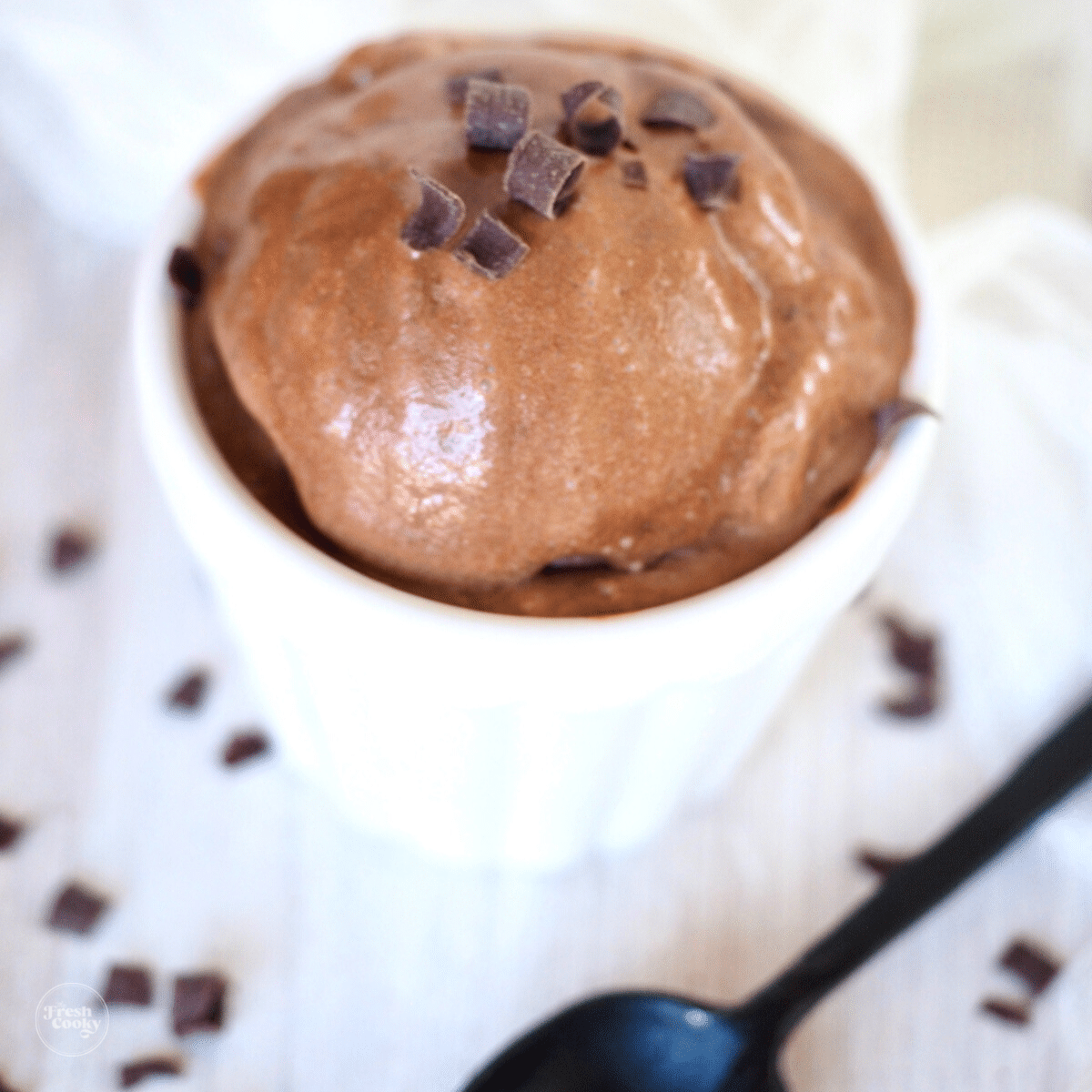 homemade chocolate ice cream recipe no eggs with scoop in white container with black spoon and chocolate curls on top.