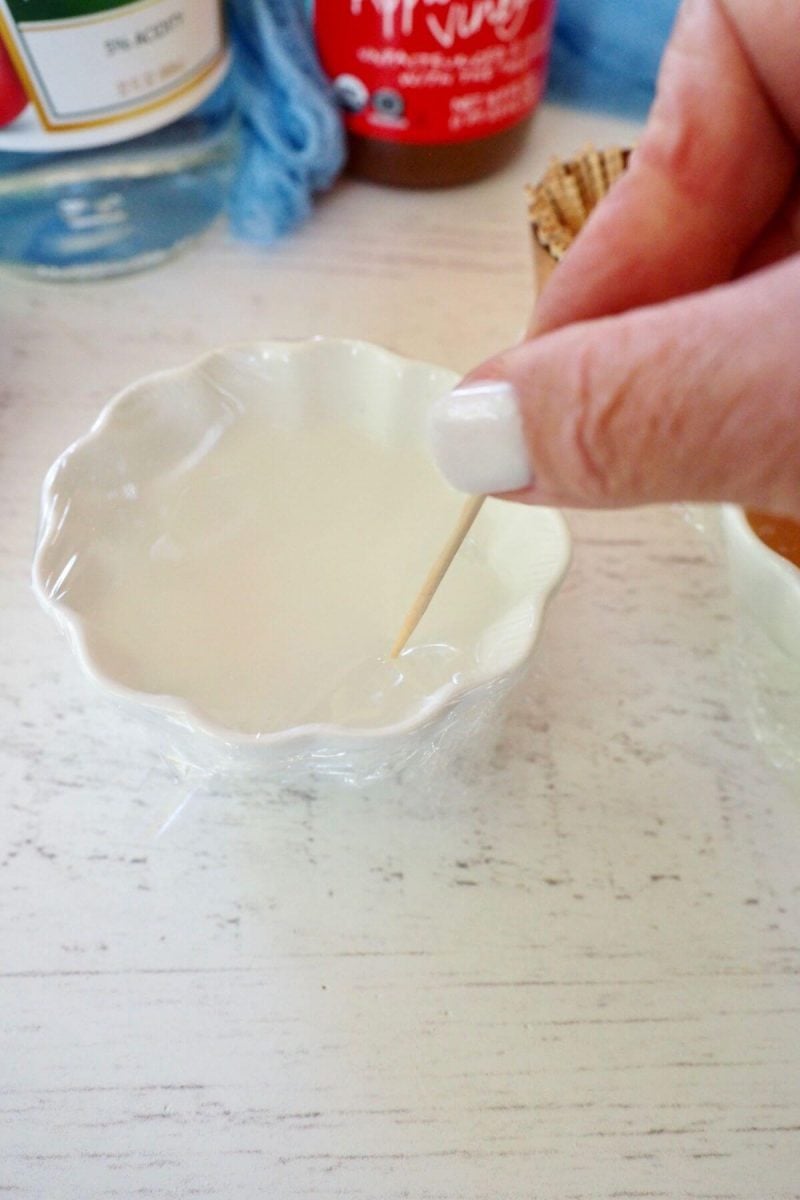Poking holes in plastic wrap using regular white vinegar for fruit fly trap.