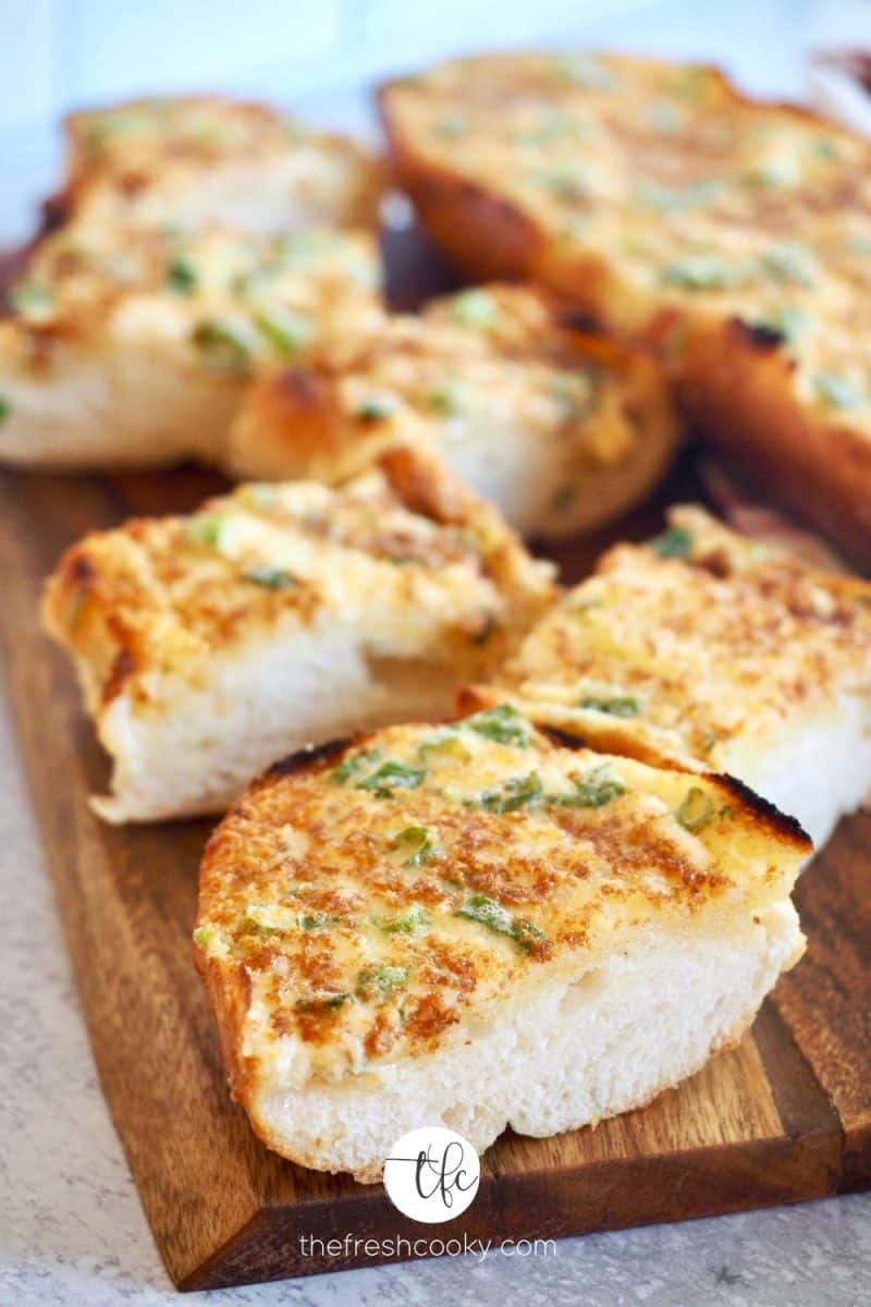 Sliced pieces of cheesy garlic bread on cutting board.