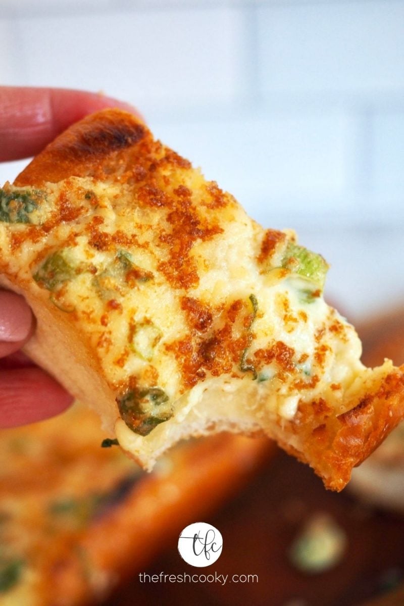 Hand holding a slice with bite taken out of cheesy bread.