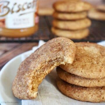 Cookie Butter Snicker doodles on a plate with a jar of cookie butter in background and stacks of cookies one with a bite taken out to reveal a gooey, chewy center.