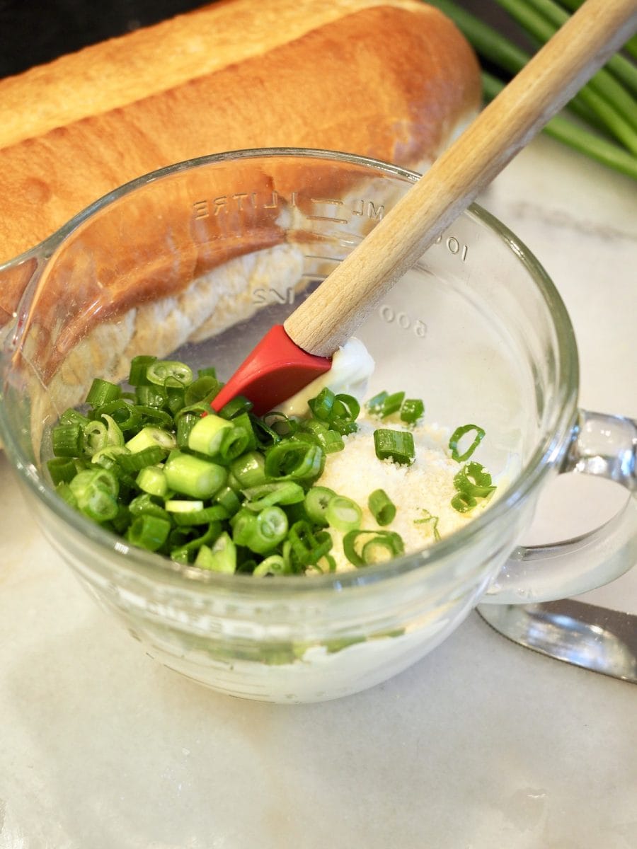 Mayo, parm cheese, sliced green onions in mixing bowl with red spatula and loaf of french bread| thefreshcooky.com
