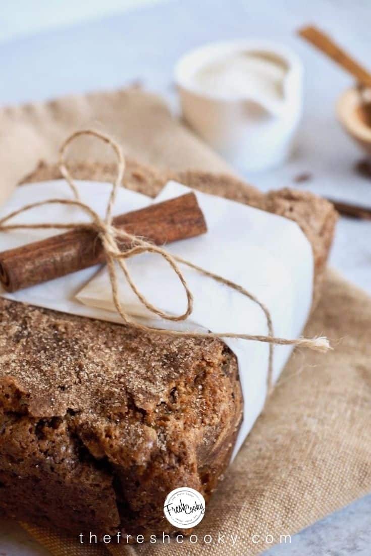 Loaf of Healthy Zucchini Bread wrapped in a strip of parchment paper tied with string and decorated with a cinnamon stick. 