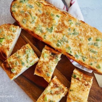 Half French bread and slices of cheesy bread on cutting board.