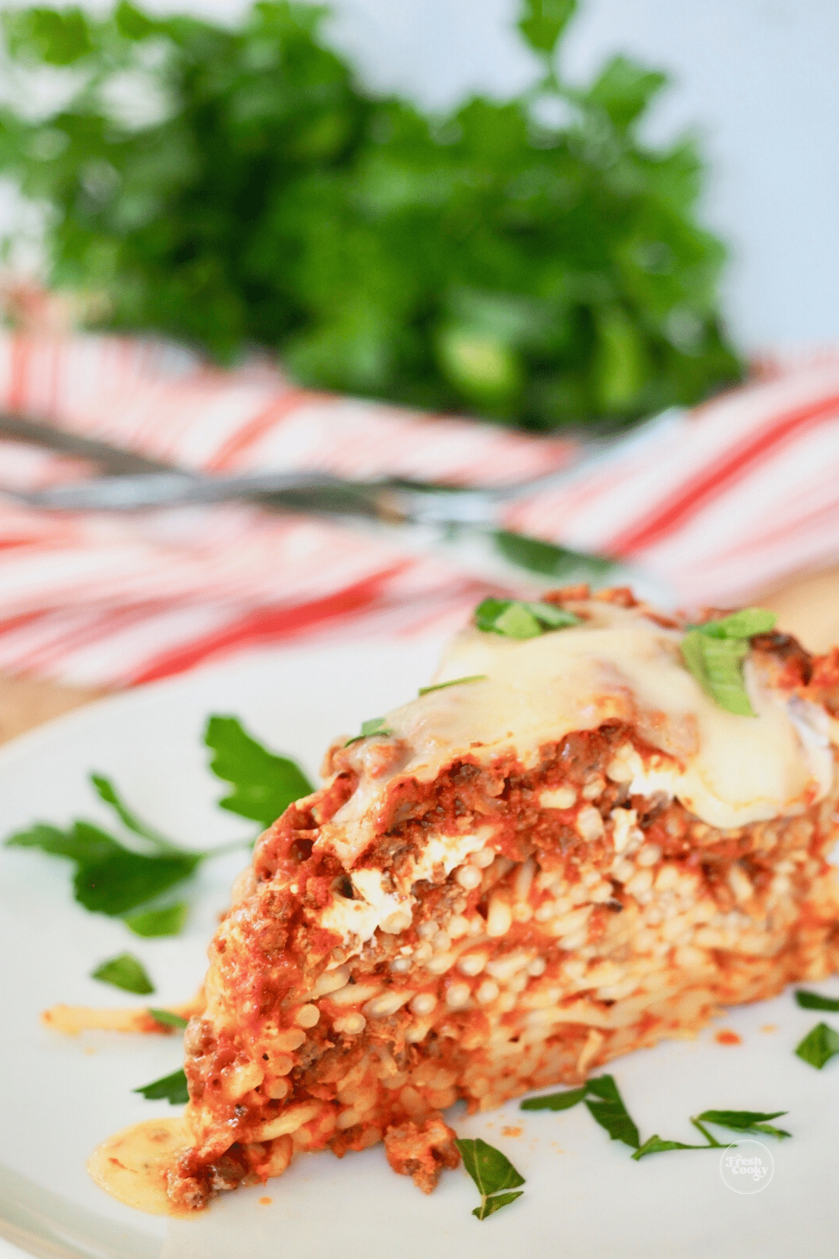 Easy baked spaghetti pie slice on plate with parsley garnish. 