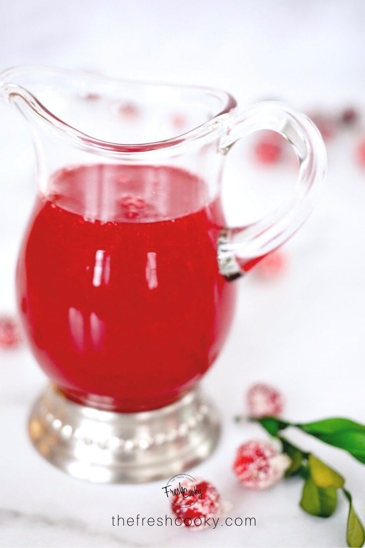 Image of small pitcher filled with cranberry simple syrup and frosted cranberries.