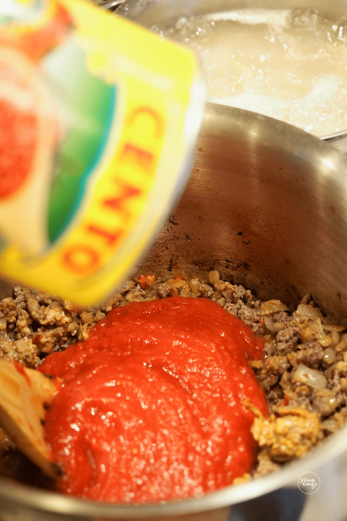Adding crushed tomatoes to the meat mixture.